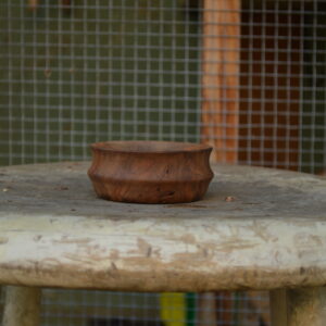 A pinch bowl with a decorative shape sits on a stool. The bowl has been hand-crafted from reclaimed Bay Area California walnut and devoid of finish for a natural look