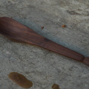 A close-up of a hand-carved reclaimed walnut hardwood teaspoon or baby spoon with a decorative teardrop handle, finished with food-safe mineral oil