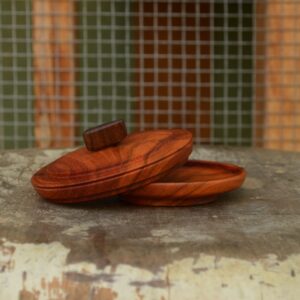 A shallow carob wood container complete with a decorative lid, hand-turned on a lathe and finished with a reclaimed Bay Area walnut handle.