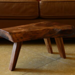 A live-edge walnut slab low side table handcrafted with Japanese-inspired joinery with three maple wood legs in a mid-century style sits in a living room.